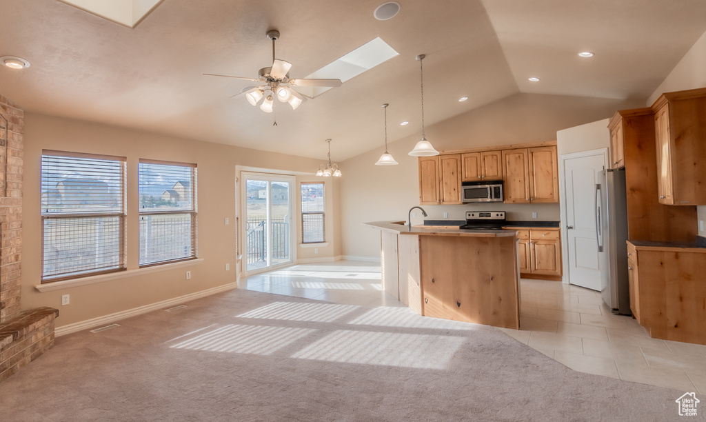 Kitchen with stainless steel appliances, a sink, light tile patterned flooring, vaulted ceiling with skylight, and light carpet