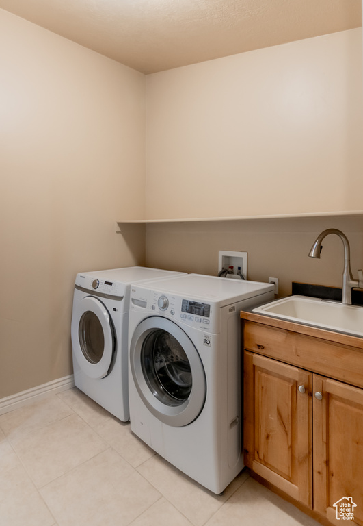 Laundry area featuring washing machine and dryer, cabinet space, a sink, and light tile patterned floors
