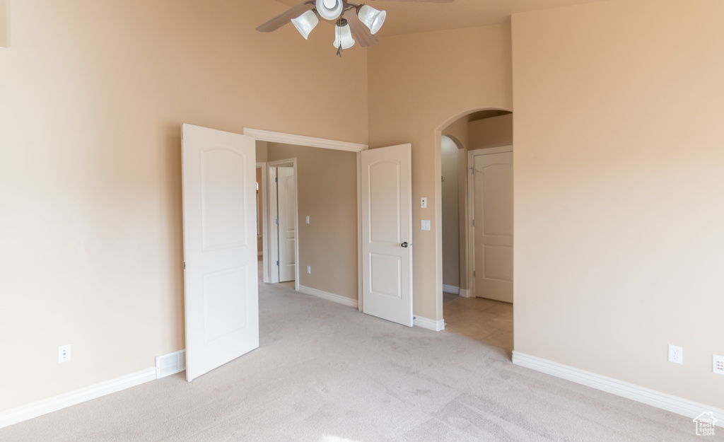 Unfurnished bedroom with arched walkways, a high ceiling, baseboards, and light colored carpet