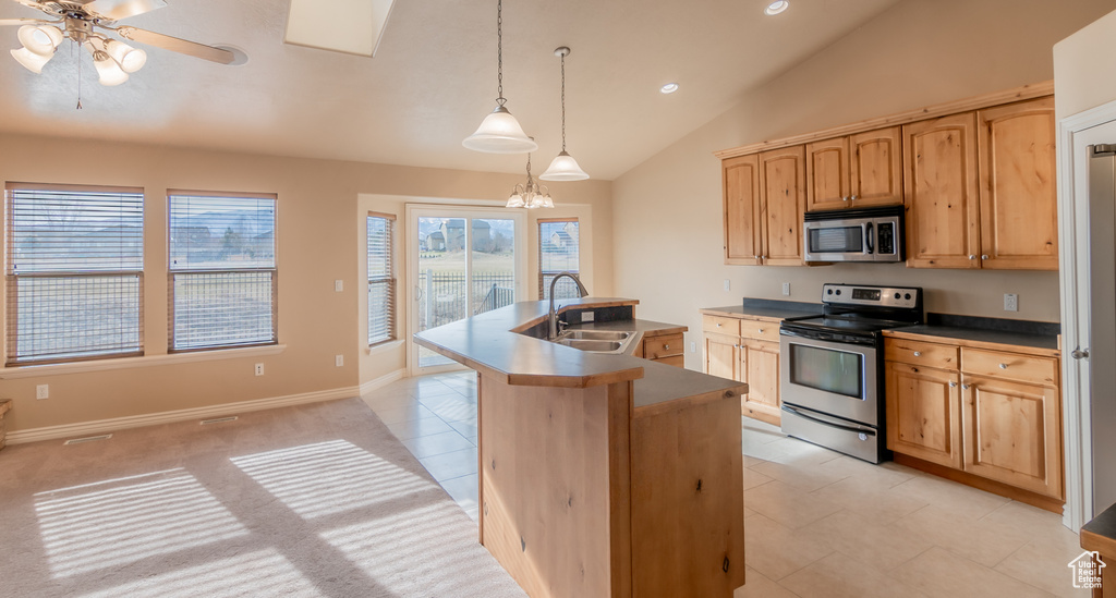 Kitchen featuring vaulted ceiling, ceiling fan with notable chandelier, a sink, an island with sink, and appliances with stainless steel finishes