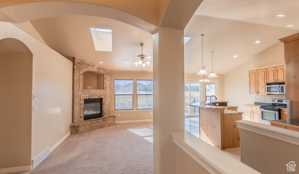 Kitchen featuring lofted ceiling with skylight, stainless steel appliances, light brown cabinetry, visible vents, and a fireplace