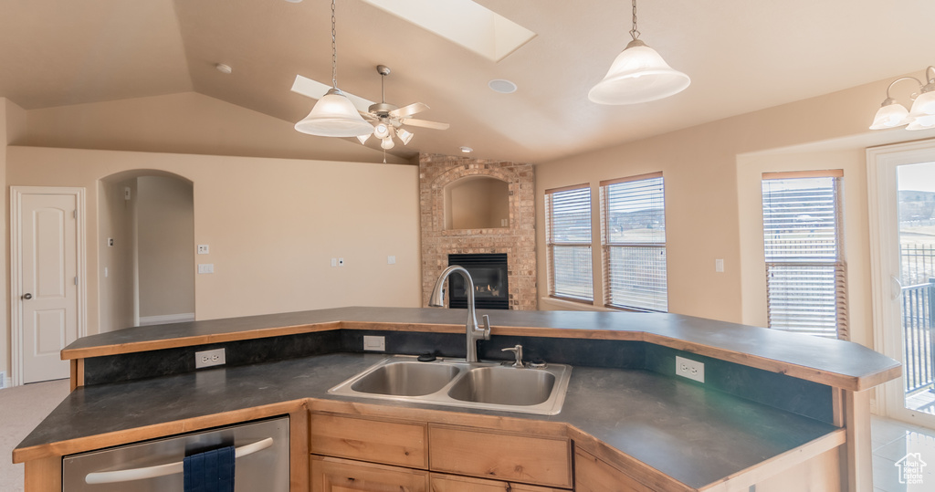 Kitchen with a sink, stainless steel dishwasher, open floor plan, dark countertops, and lofted ceiling with skylight