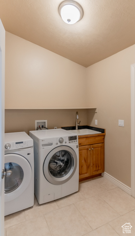 Washroom featuring light tile patterned floors, baseboards, washing machine and clothes dryer, a sink, and cabinet space