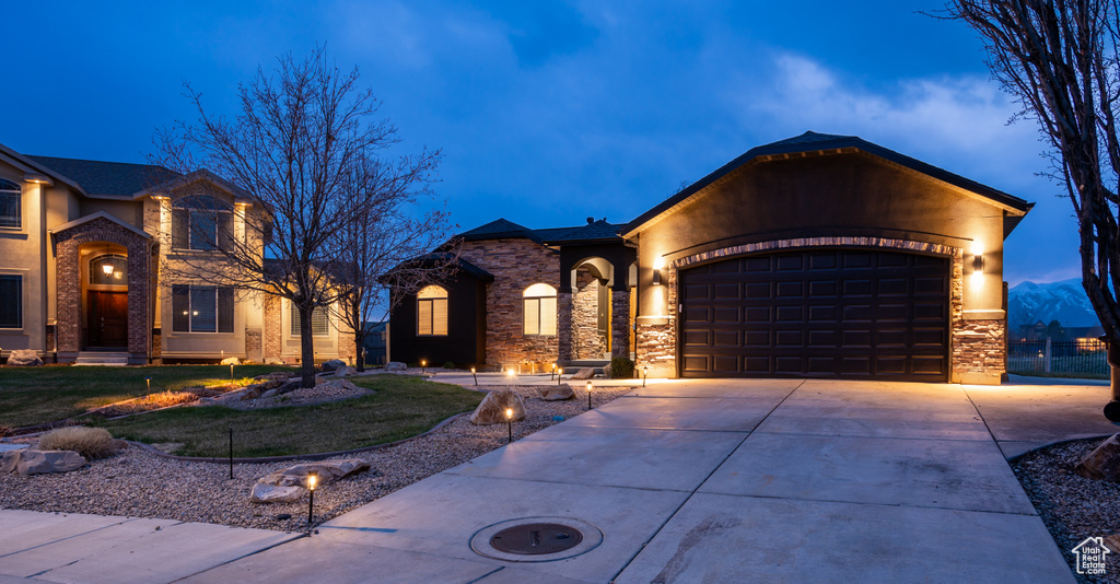 View of front of property featuring driveway, a front yard, stone siding, and a garage