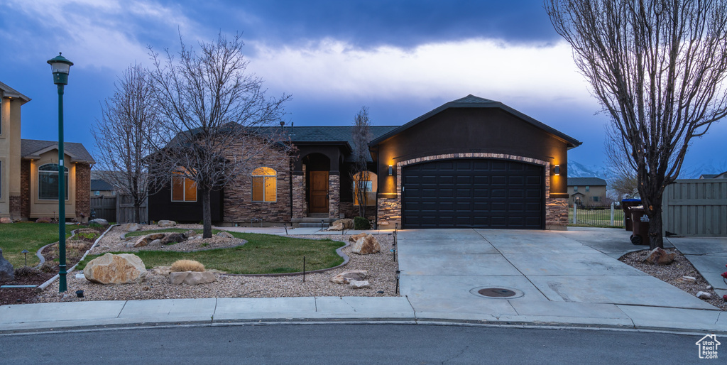 View of front of house featuring stone siding, driveway, a garage, and fence