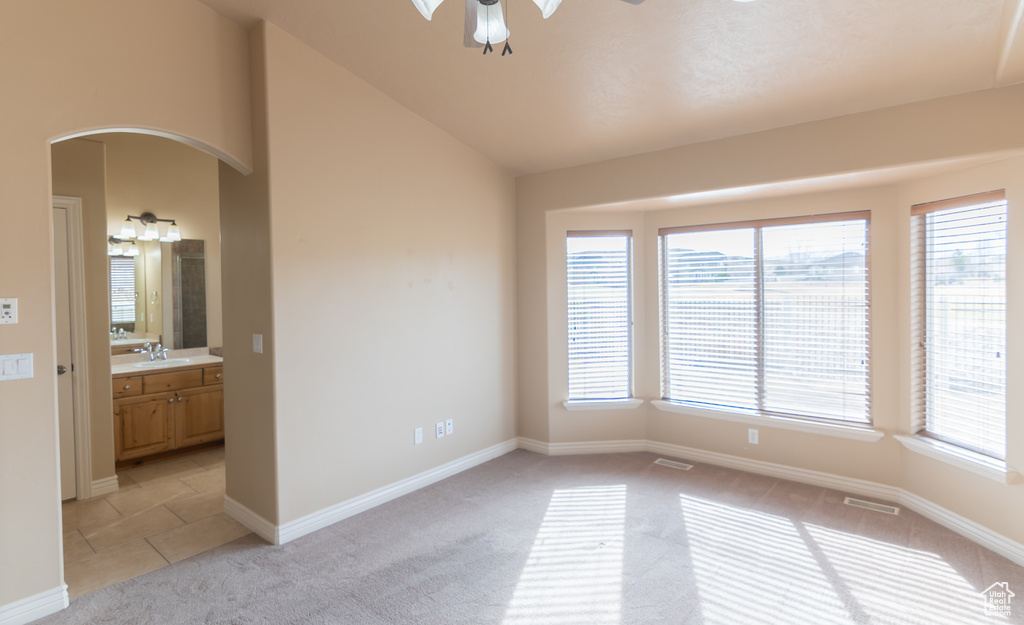 Unfurnished room featuring a ceiling fan, lofted ceiling, light colored carpet, visible vents, and arched walkways