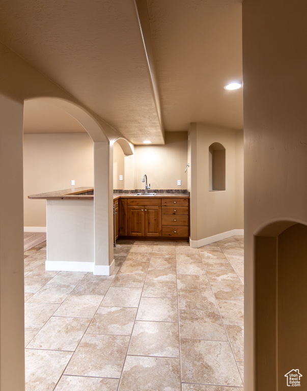 Kitchen featuring a sink, a peninsula, baseboards, and brown cabinets