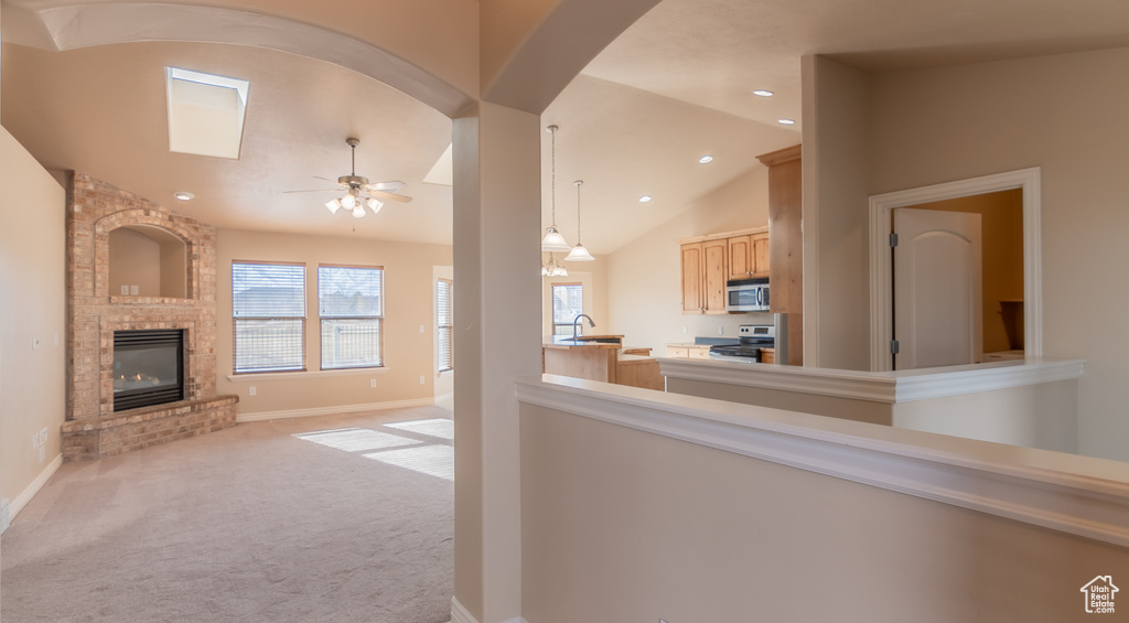Interior space featuring baseboards, a fireplace, a ceiling fan, vaulted ceiling, and light colored carpet