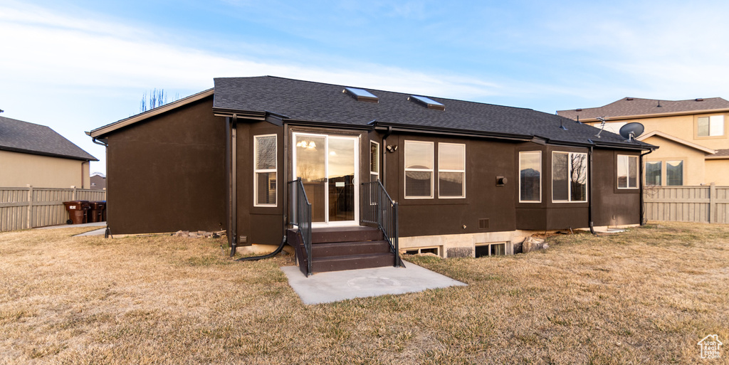 Back of property featuring fence, roof with shingles, and a yard