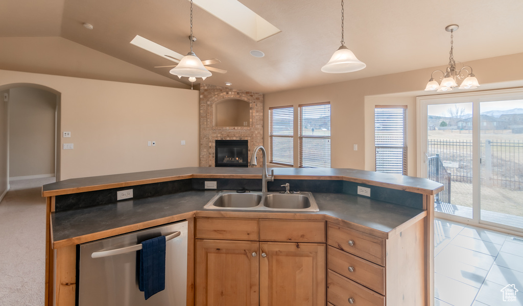 Kitchen with open floor plan, lofted ceiling with skylight, stainless steel dishwasher, a sink, and a brick fireplace