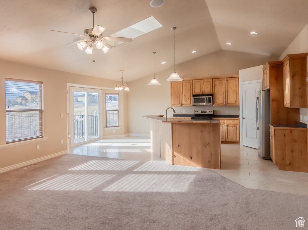 Kitchen with light carpet, light tile patterned flooring, vaulted ceiling with skylight, and stainless steel appliances
