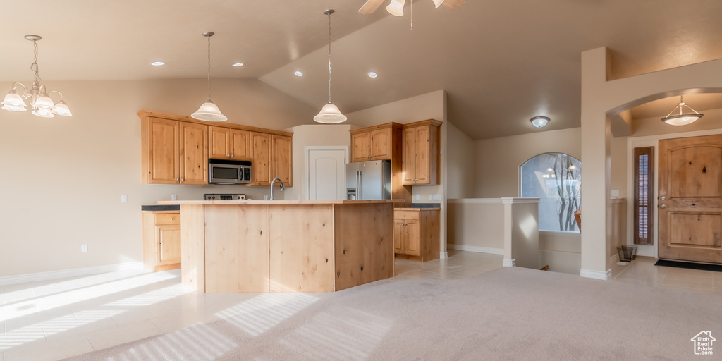 Kitchen with arched walkways, an island with sink, decorative light fixtures, and appliances with stainless steel finishes