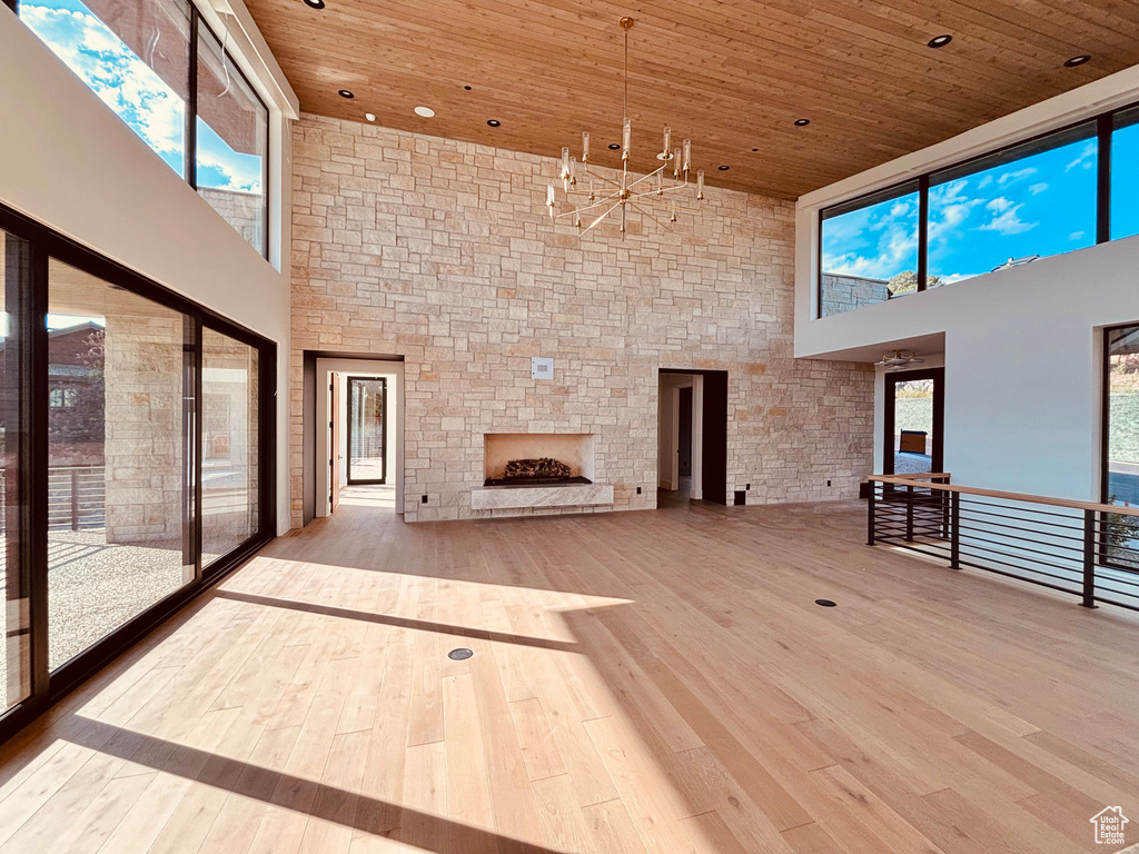 Unfurnished living room with a high ceiling, wooden ceiling, a stone fireplace, hardwood / wood-style floors, and a chandelier