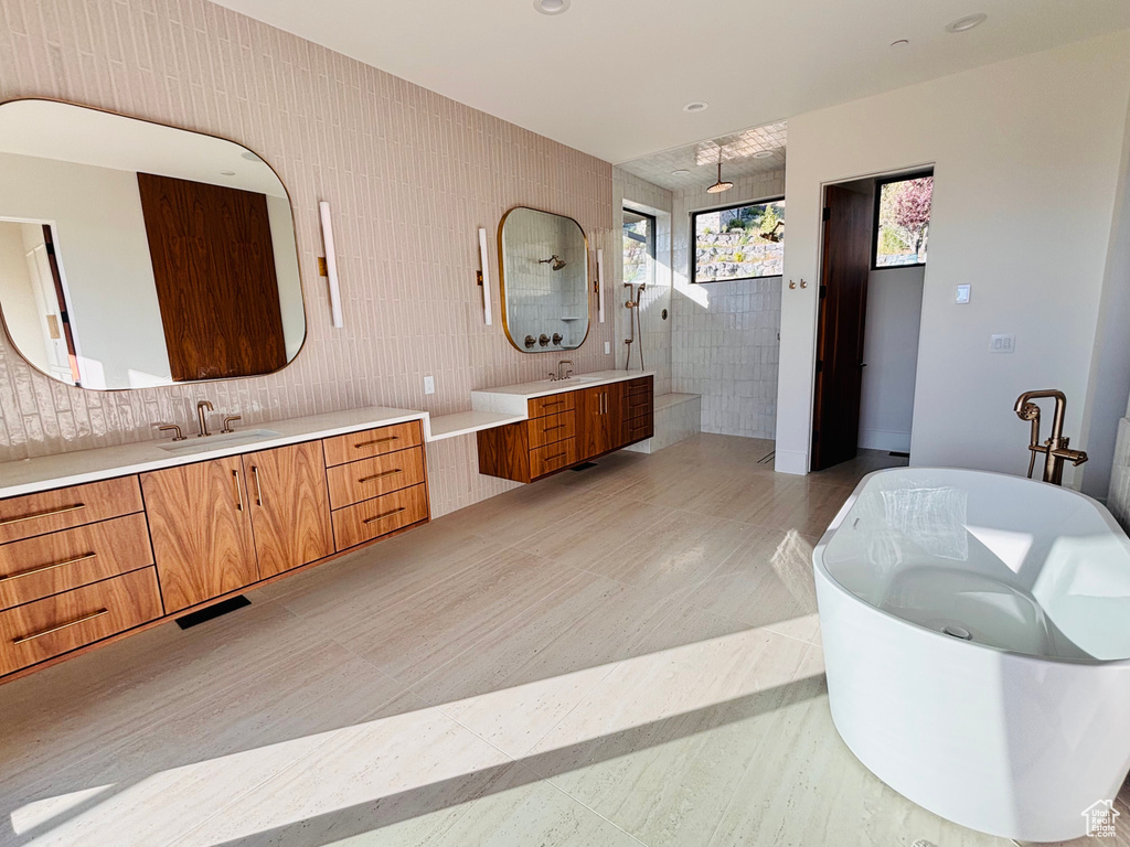 Full bathroom featuring a walk in shower, a soaking tub, two vanities, tile patterned floors, and tile walls