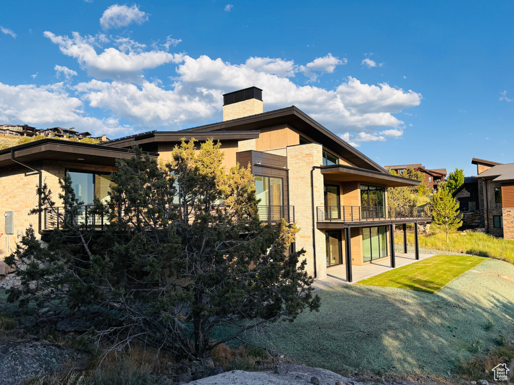Back of property featuring a chimney, a patio area, and a balcony