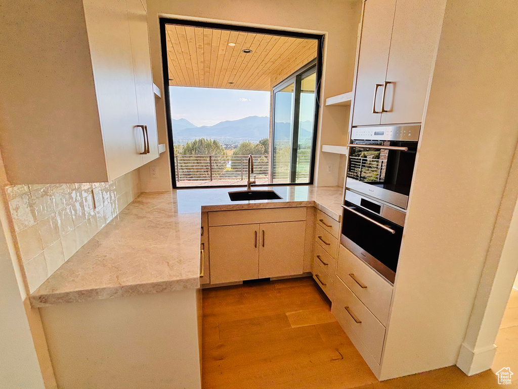 Kitchen featuring decorative backsplash, light wood finished floors, a wall of windows, wooden ceiling, and a mountain view
