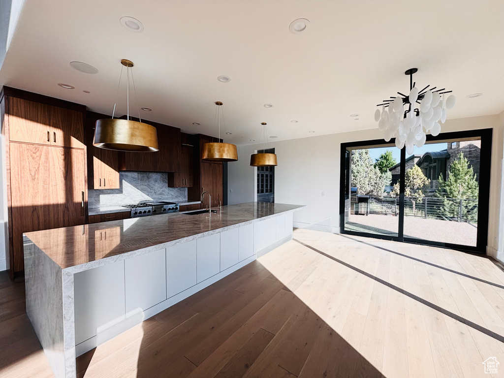 Kitchen featuring modern cabinets, wood finished floors, a spacious island, decorative backsplash, and decorative light fixtures