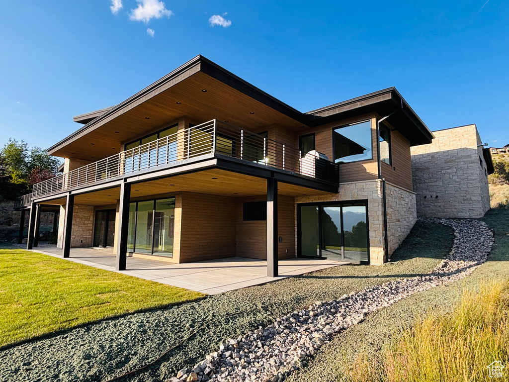 Back of house with stone siding, a patio area, and a lawn