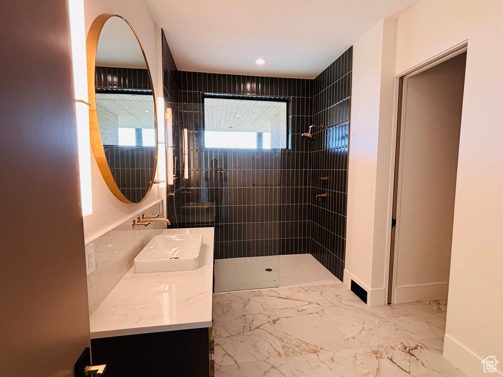Full bath featuring a tile shower, double vanity, and marble finish flooring