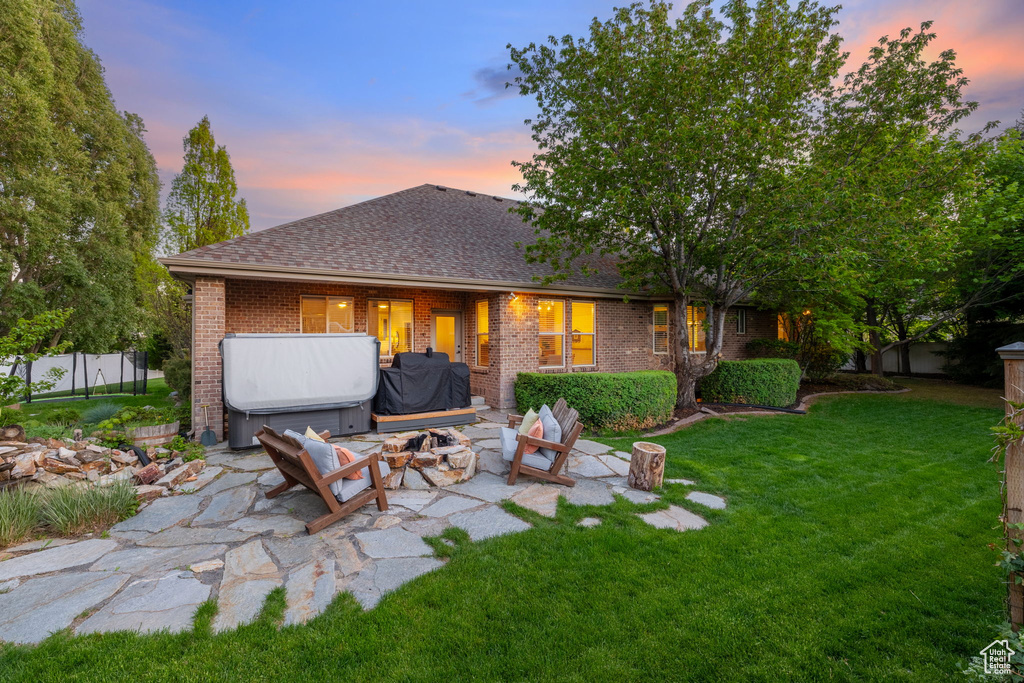 Back of house at dusk with brick siding, a shingled roof, an outdoor fire pit, and a patio area