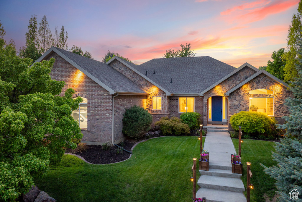 View of front of home featuring a front lawn, brick siding, a shingled roof, and stone siding