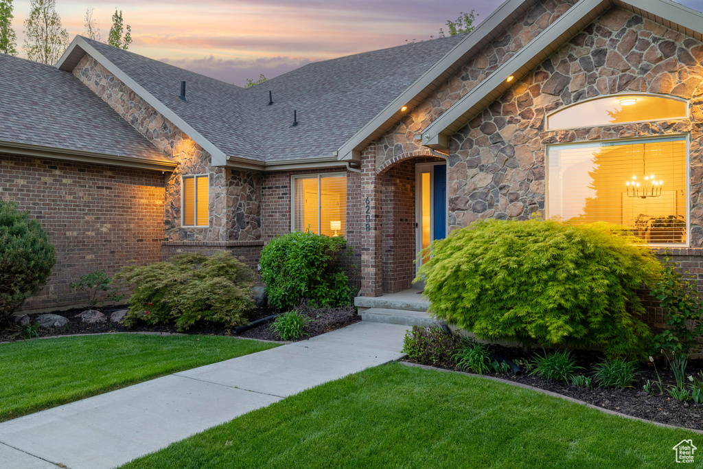 View of front of home with a lawn, a shingled roof, brick siding, and stone siding
