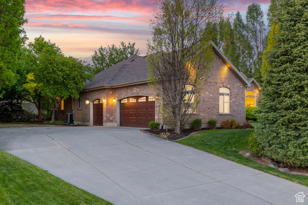 View of front of house with brick siding, an attached garage, concrete driveway, a lawn, and central air condition unit