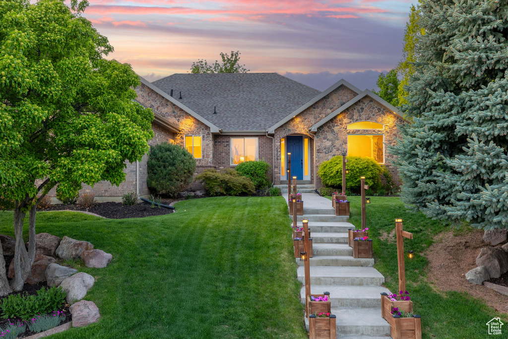 View of front of house with a lawn, roof with shingles, brick siding, and stone siding