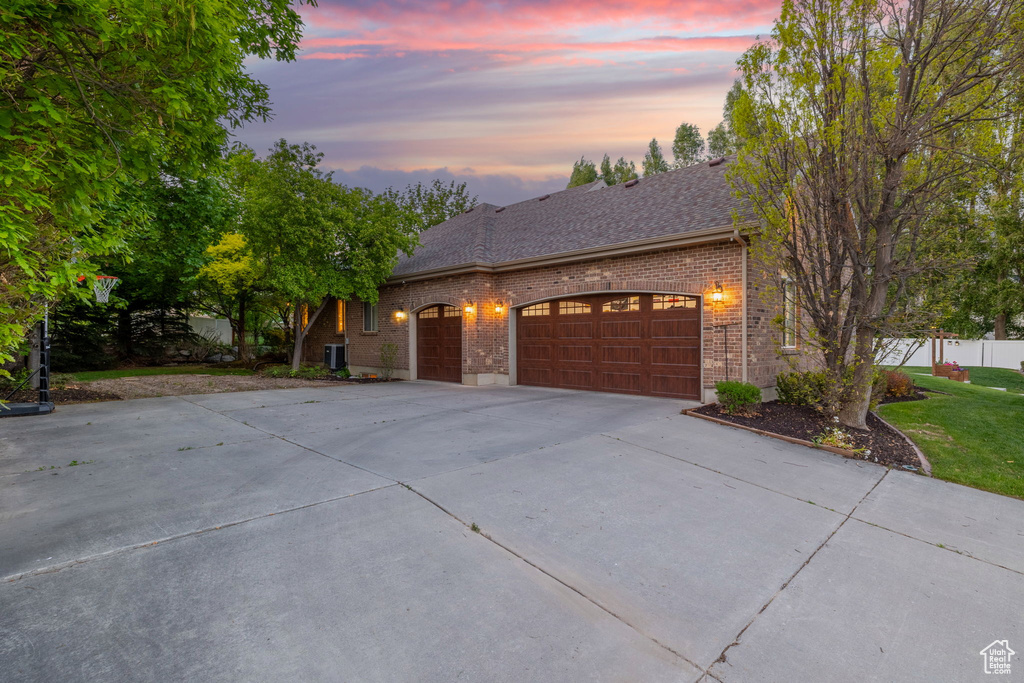 View of front of property with concrete driveway, brick siding, a garage, a shingled roof, and a yard
