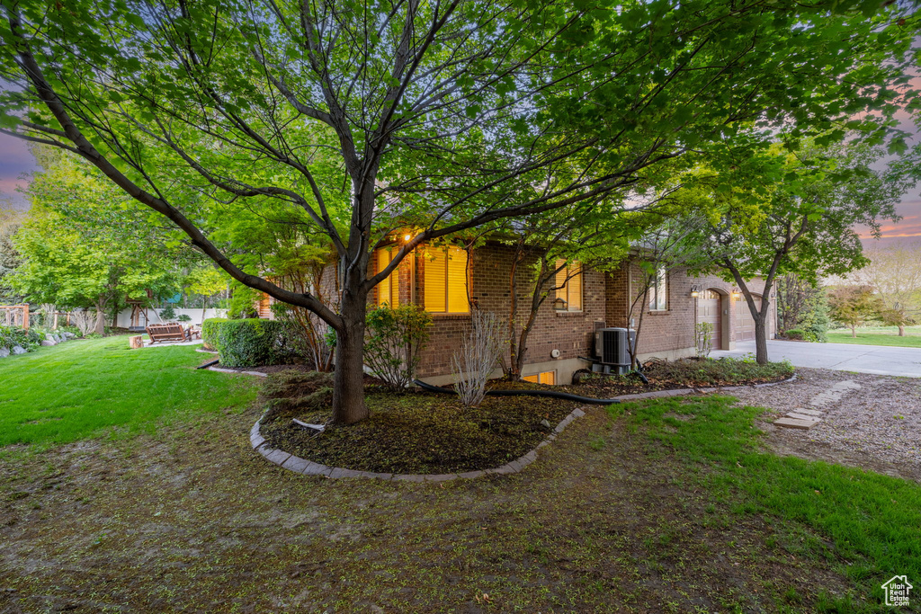 View of front of property featuring central AC, brick siding, driveway, a front yard, and an attached garage