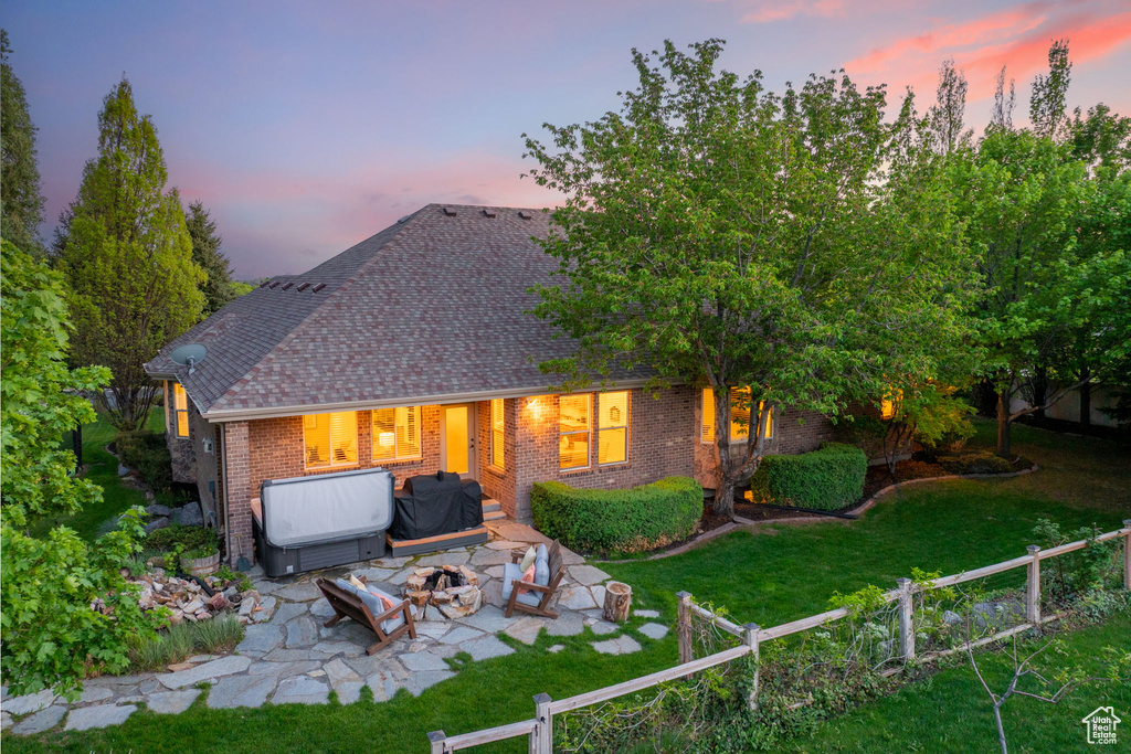 Back of house at dusk with an outdoor fire pit, a patio area, brick siding, and a shingled roof