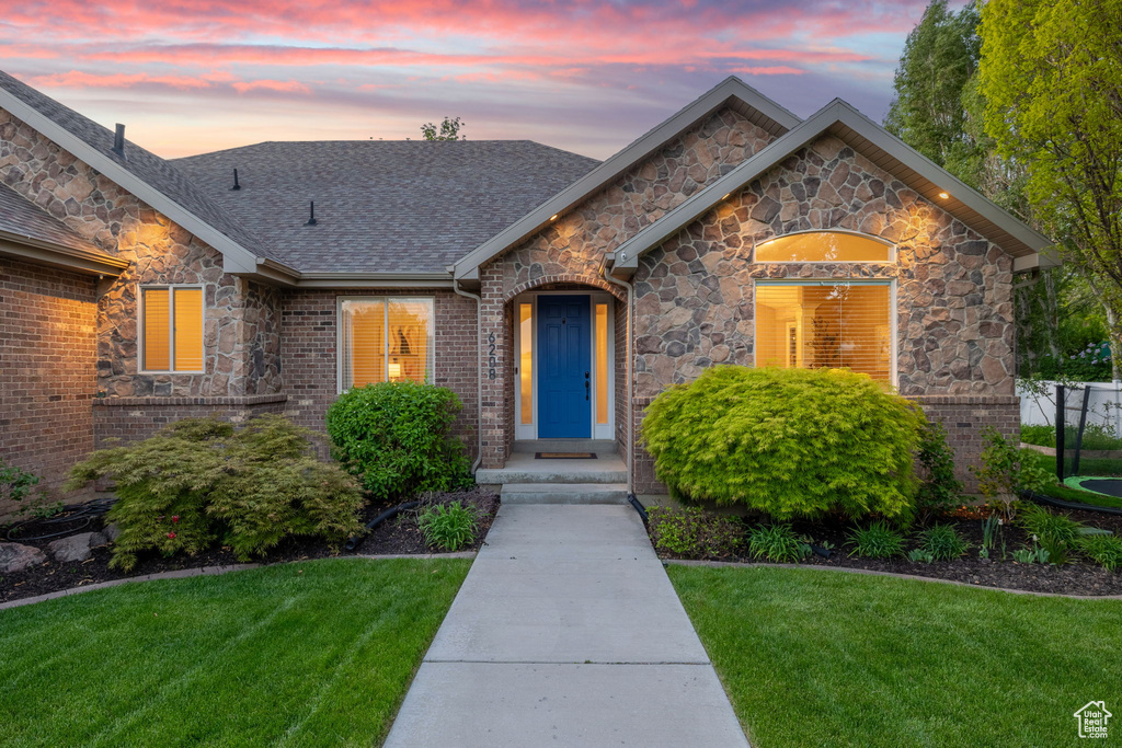 View of front of property with a front yard, a shingled roof, and stone siding
