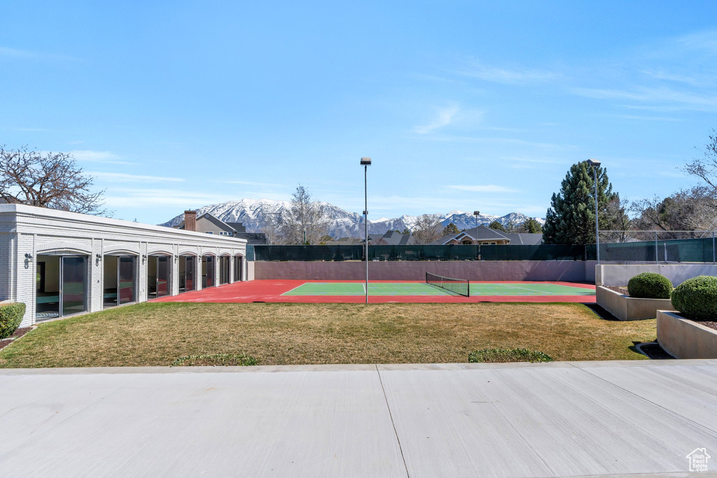 Surrounding community featuring a tennis court, a mountain view, fence, and a lawn