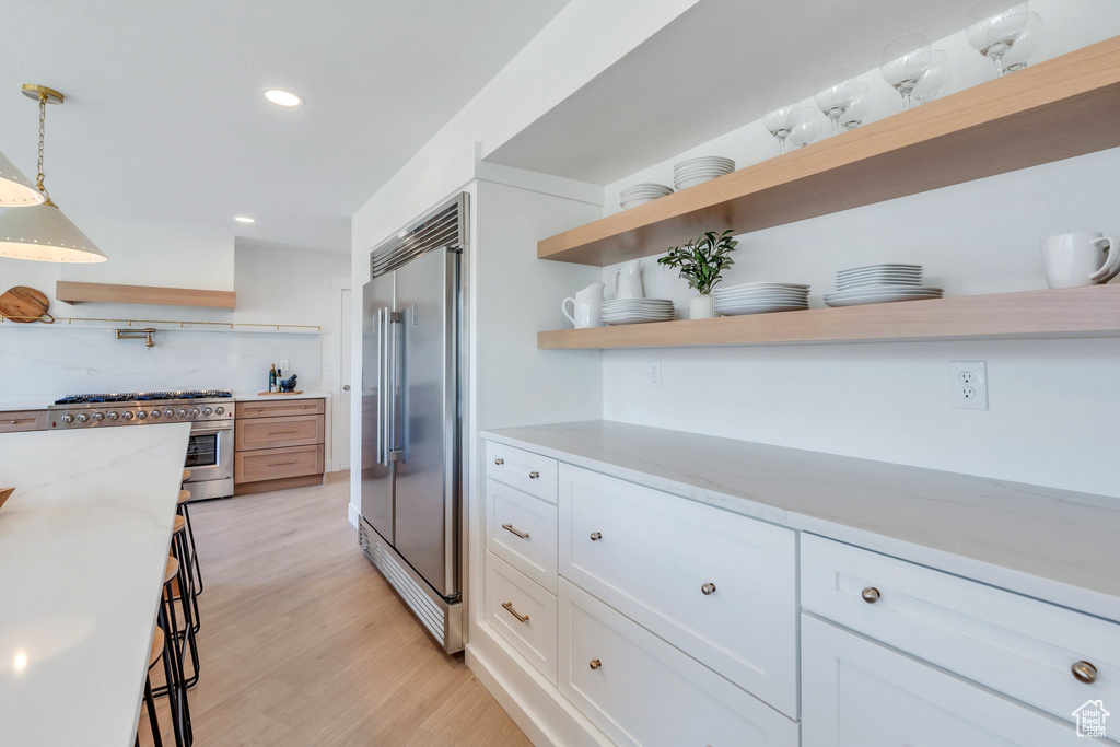 Kitchen featuring white cabinets, high quality appliances, light wood finished floors, and open shelves