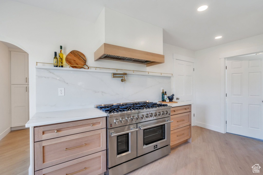 Kitchen featuring double oven range, arched walkways, light wood-style flooring, and decorative backsplash