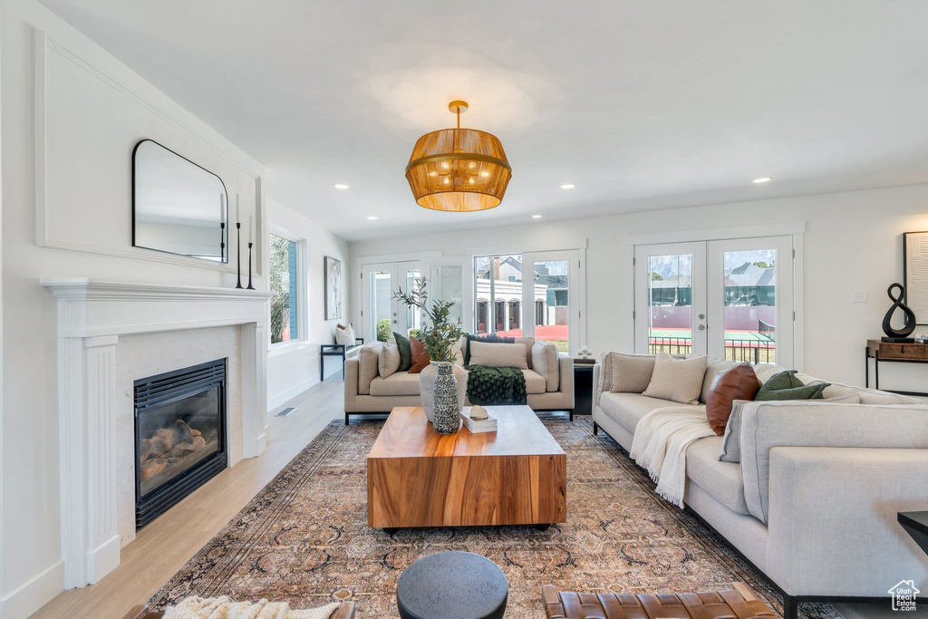 Living area featuring french doors, a glass covered fireplace, plenty of natural light, and light wood finished floors