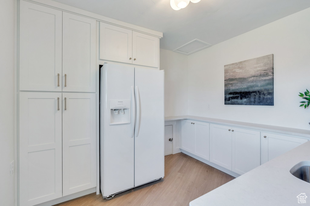 Kitchen featuring light wood-type flooring, light countertops, white fridge with ice dispenser, and white cabinets
