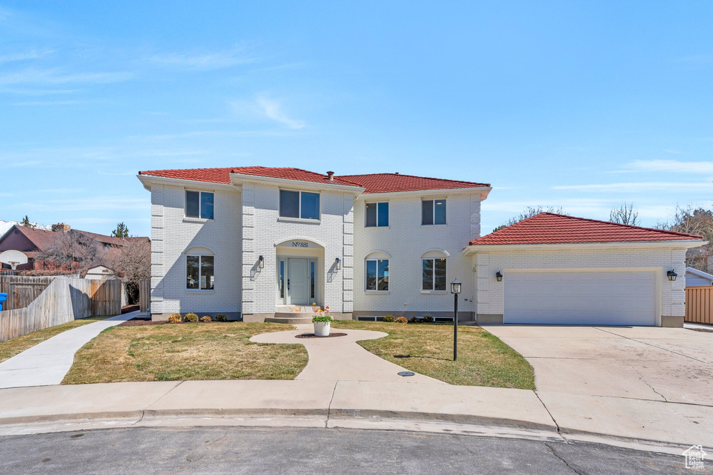 Mediterranean / spanish home featuring driveway, a tile roof, fence, a front lawn, and a garage