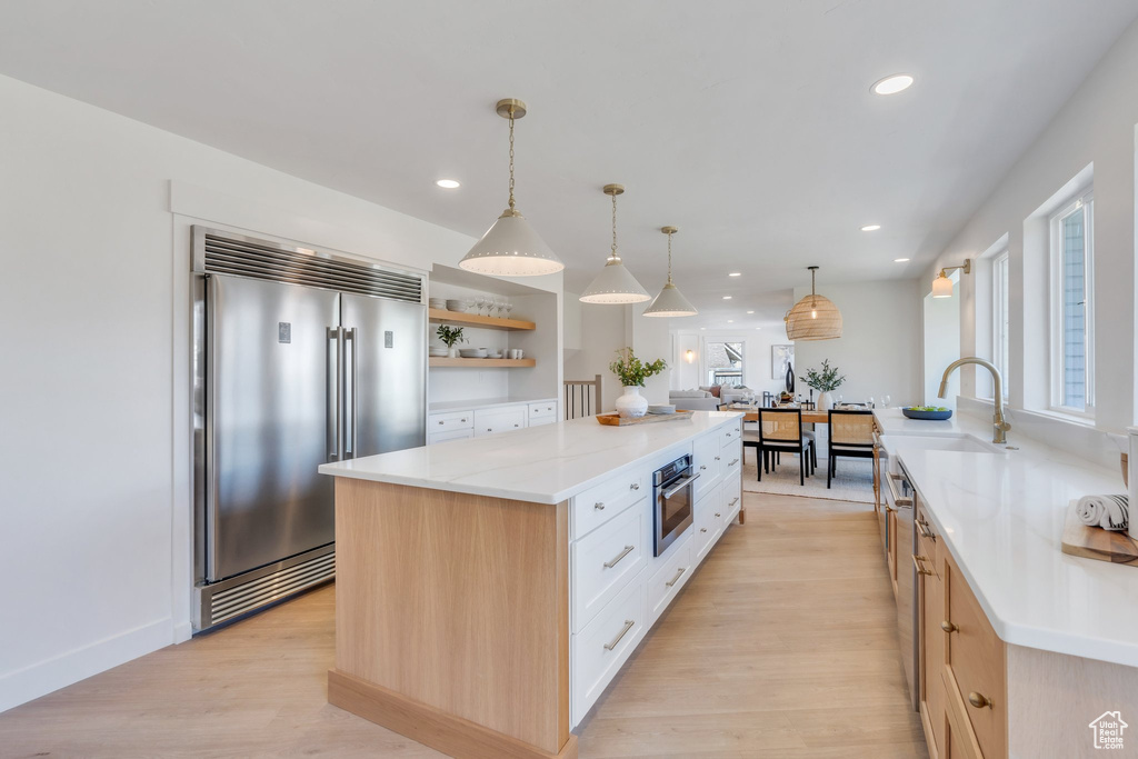 Kitchen featuring open shelves, a center island, stainless steel appliances, a sink, and light wood-style floors
