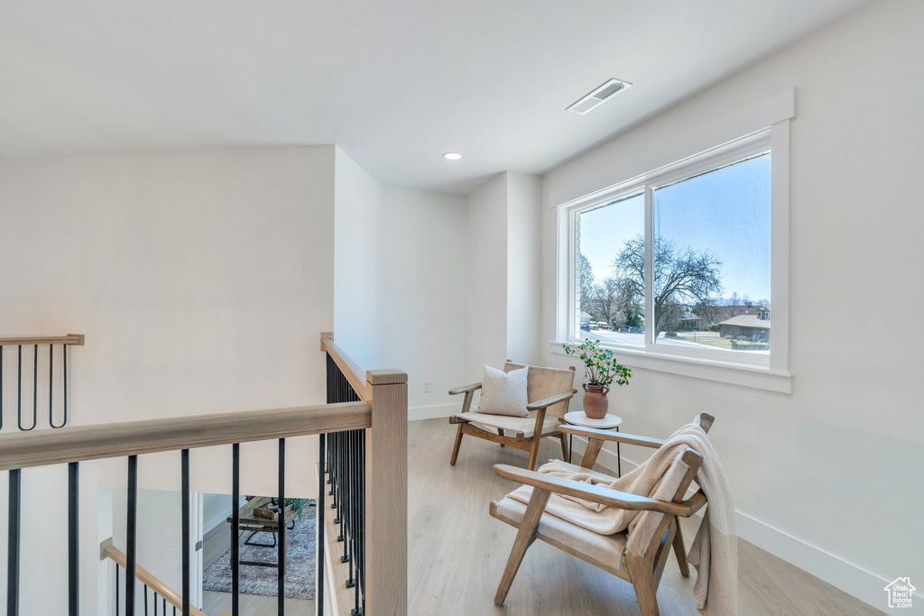 Sitting room with baseboards, visible vents, an upstairs landing, and light wood-style flooring