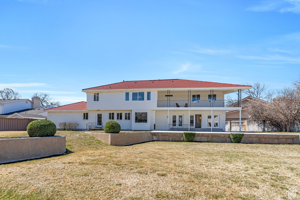 Back of property featuring a balcony, a tile roof, french doors, a yard, and a patio area