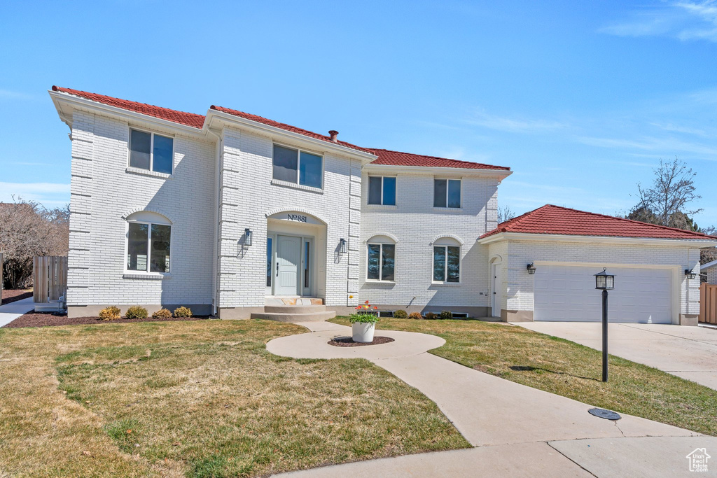 Mediterranean / spanish house with driveway, an attached garage, a front lawn, and brick siding