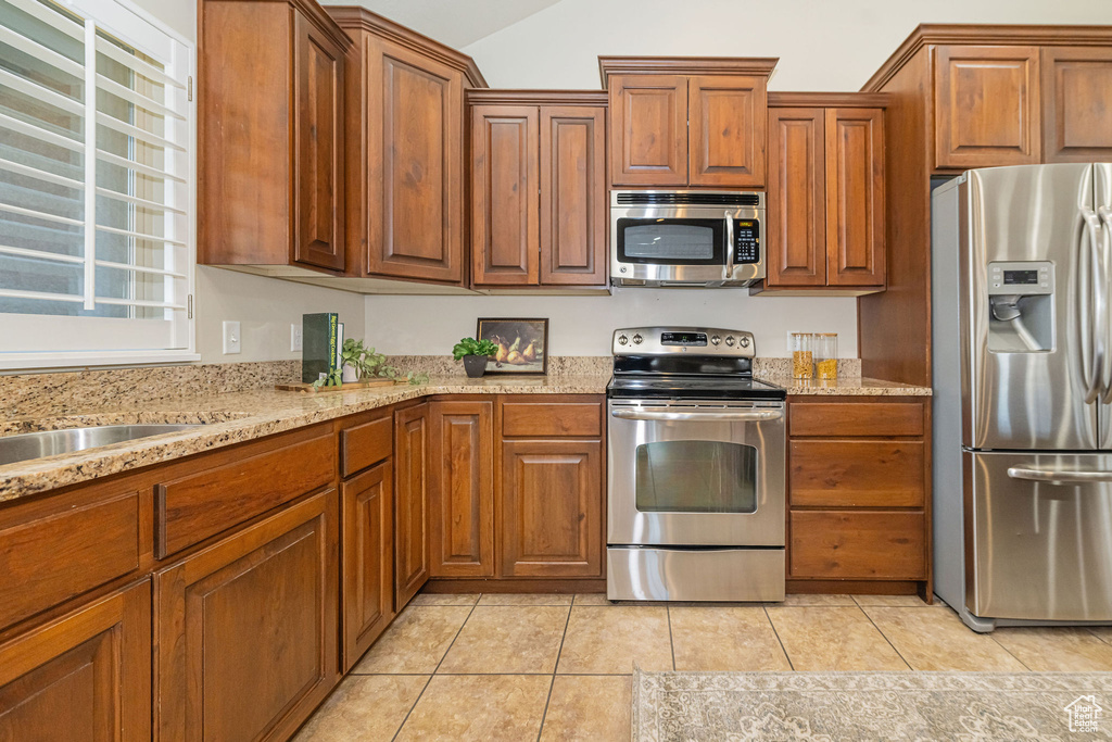 Kitchen featuring light tile patterned flooring, brown cabinetry, and stainless steel appliances