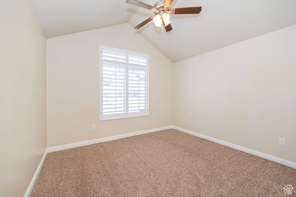 Empty room featuring baseboards, lofted ceiling, carpet, and a ceiling fan