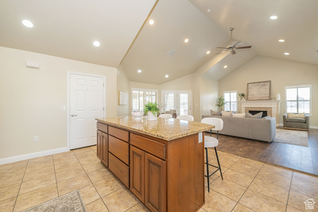 Kitchen with a breakfast bar area, a center island, light stone counters, a ceiling fan, and brown cabinetry