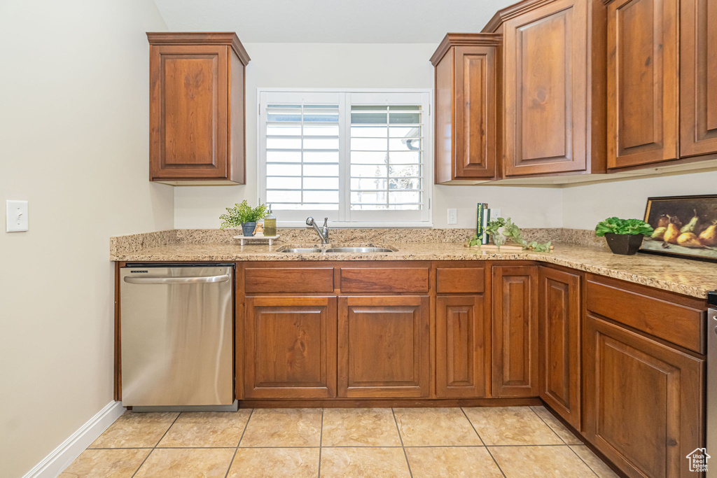 Kitchen with brown cabinets, a sink, light stone counters, stainless steel dishwasher, and light tile patterned floors