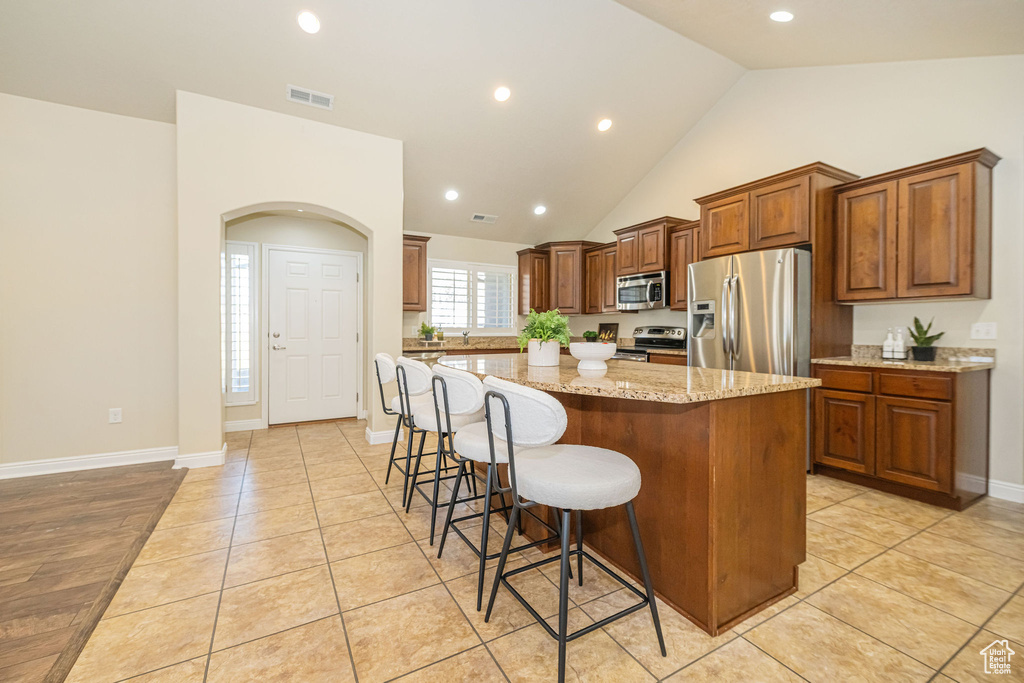 Kitchen featuring a center island, a breakfast bar, visible vents, light stone countertops, and appliances with stainless steel finishes