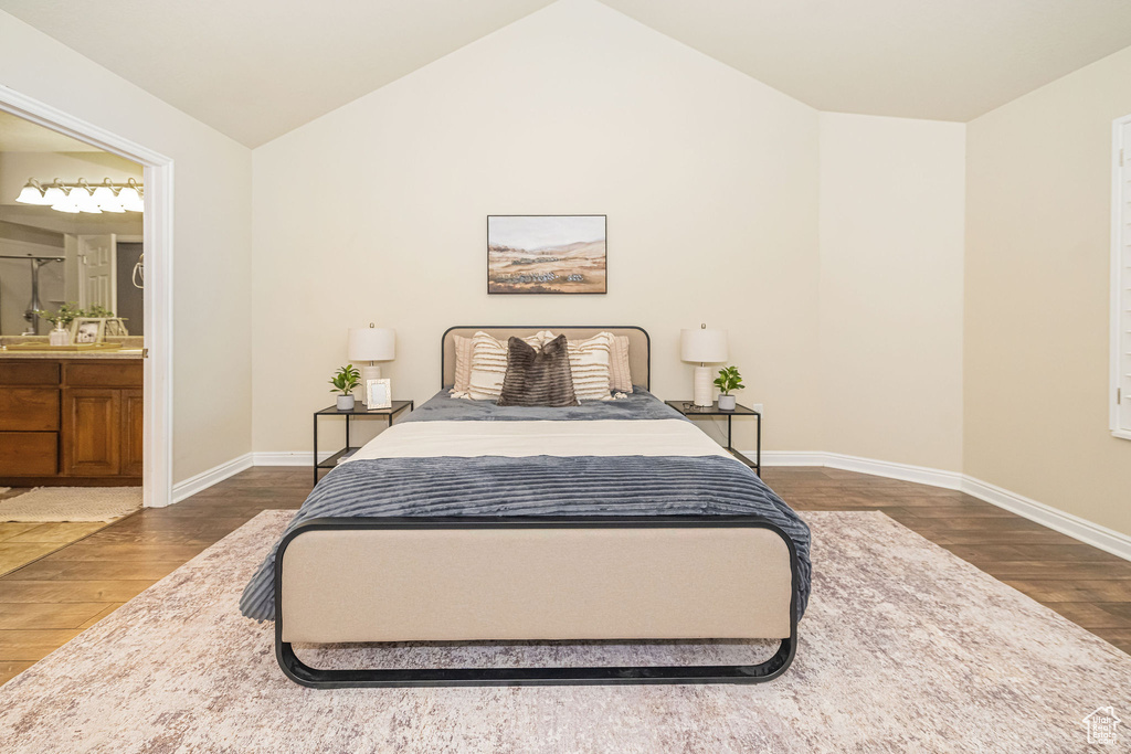 Bedroom featuring ensuite bathroom, baseboards, vaulted ceiling, and wood finished floors