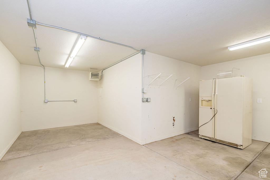 Garage with white refrigerator with ice dispenser and baseboards