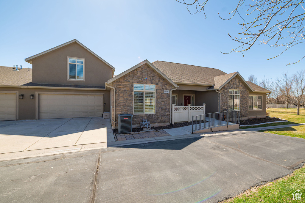 View of front of home with stone siding, central AC unit, a garage, concrete driveway, and stucco siding